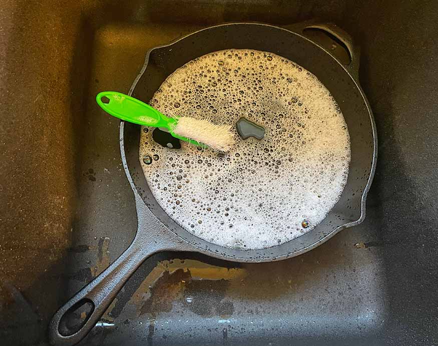 un cepillo de cerdas gruesas en una sartén de hierro fundido llena de una mezcla de agua y jabón