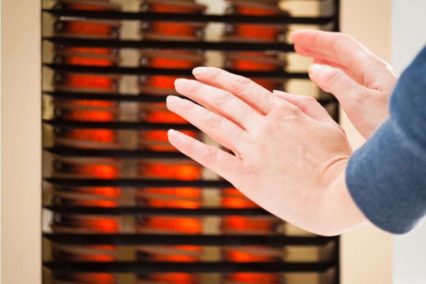manos calentándose junto a un calentador con elemento calefactor PTC